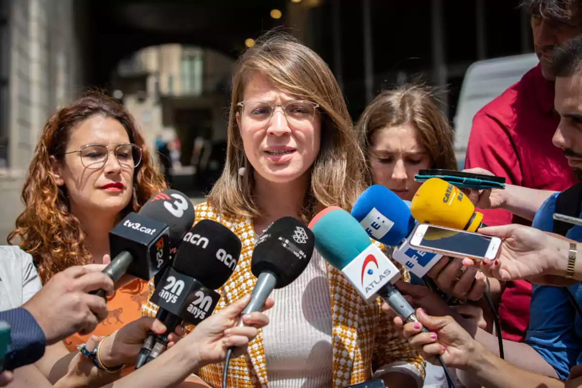 Janet Sanz, de los Comuns, hablando frente a varios micrófonos de diferentes medios de comunicación.