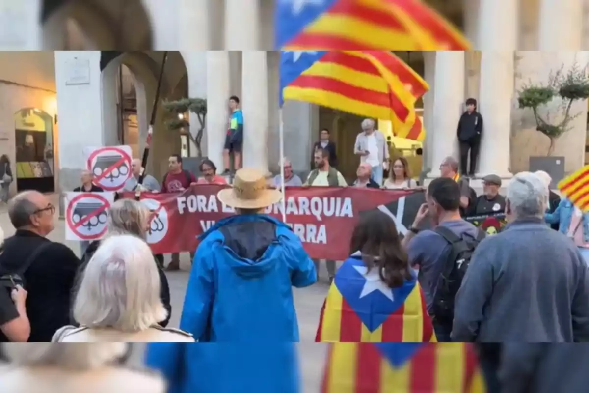 Una manifestación con personas sosteniendo una pancarta roja con un mensaje en catalán y banderas de Cataluña.