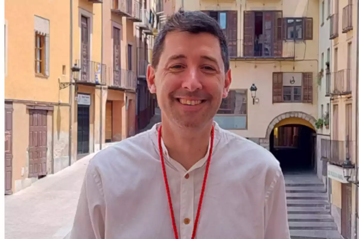 El alcalde de Berga, Ivan Sànchez i Rodriguez, sonriendo con camisa blanca y collar rojo en una calle con edificios antiguos.