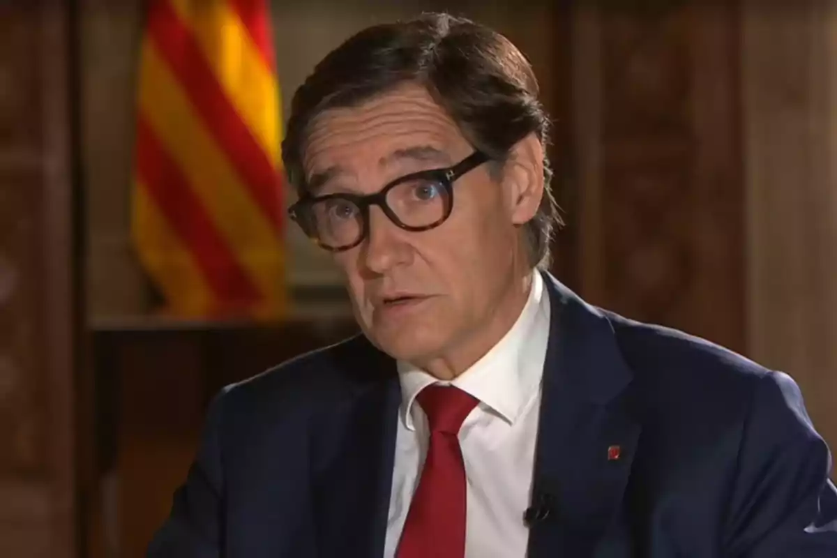 Salvador Illa, presidente de la Generalitat, dando una entrevista, con una bandera catalana en el fondo.