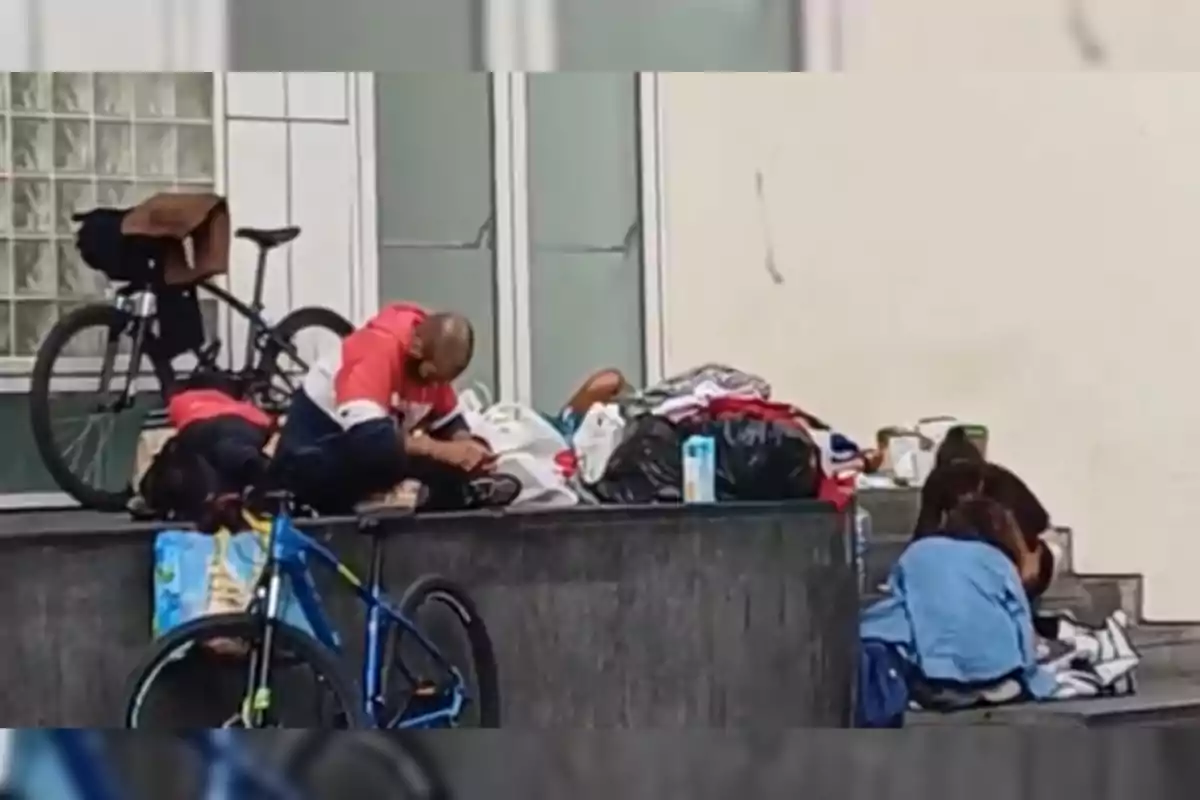 Un grupo de personas descansa en una acera junto a bicicletas y bolsas.