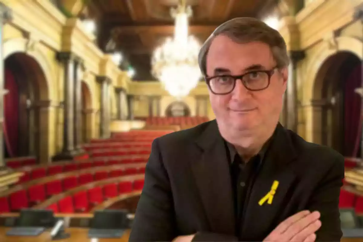 Vicent Partal, el director de VilaWeb, está de pie con los brazos cruzados en una sala con asientos rojos y un candelabro grande.