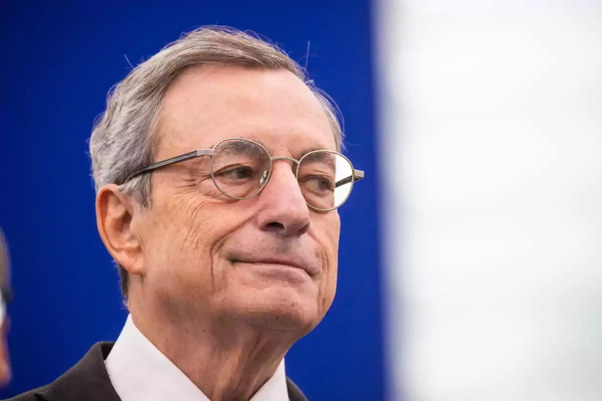 Mario Draghi mira hacia un lado con una expresión seria y un fondo azul.