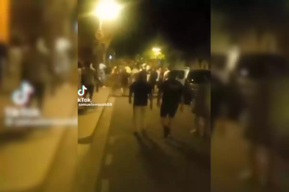 Una multitud de personas caminando por una calle iluminada por farolas durante la noche.