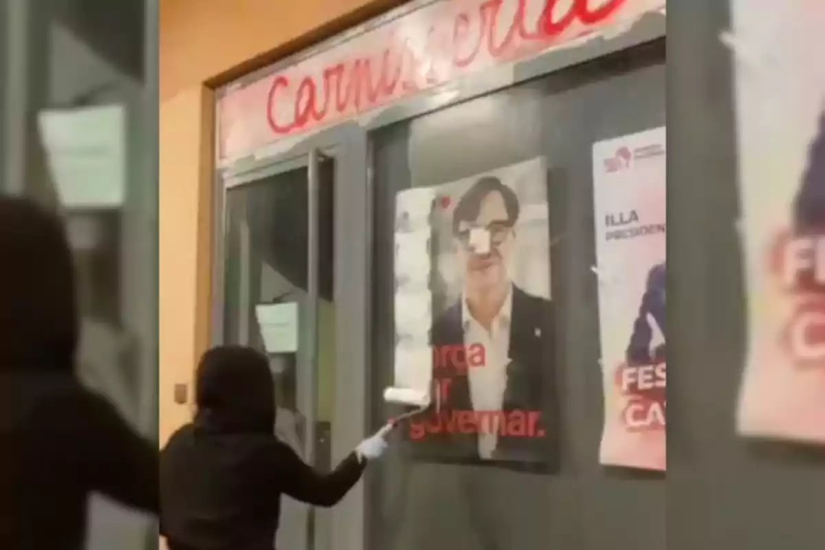 Una persona con capucha y guantes está pintando sobre un cartel en la ventana de una carnicería.