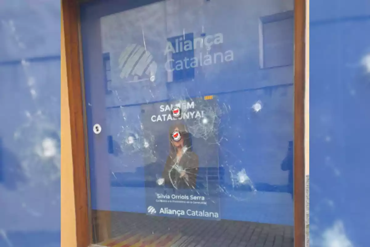 Una ventana con un cartel de Aliança Catalana que tiene varios impactos visibles.