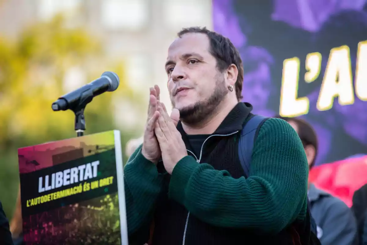 David Fernàndez hablando en un micrófono durante una manifestación con un cartel que dice "Llibertat l'autodeterminació és un dret".