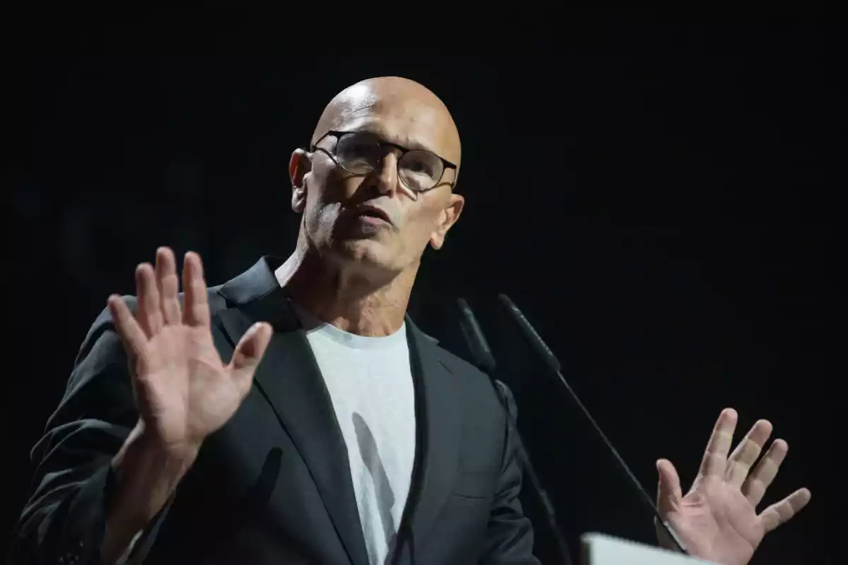 Raül Romeva gesticula mientras habla en un escenario iluminado.