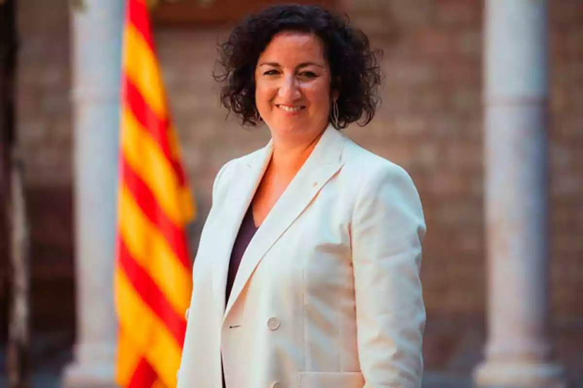 Mujer con chaqueta blanca sonriendo frente a una bandera con franjas rojas y amarillas. Mujer con chaqueta blanca sonriendo frente a una bandera con franjas rojas y amarillas.