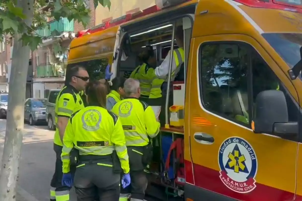 Un grupo de paramédicos con uniformes amarillos está junto a una ambulancia en una calle de Madrid. Un grupo de paramédicos con uniformes amarillos está junto a una ambulancia en una calle de Madrid.