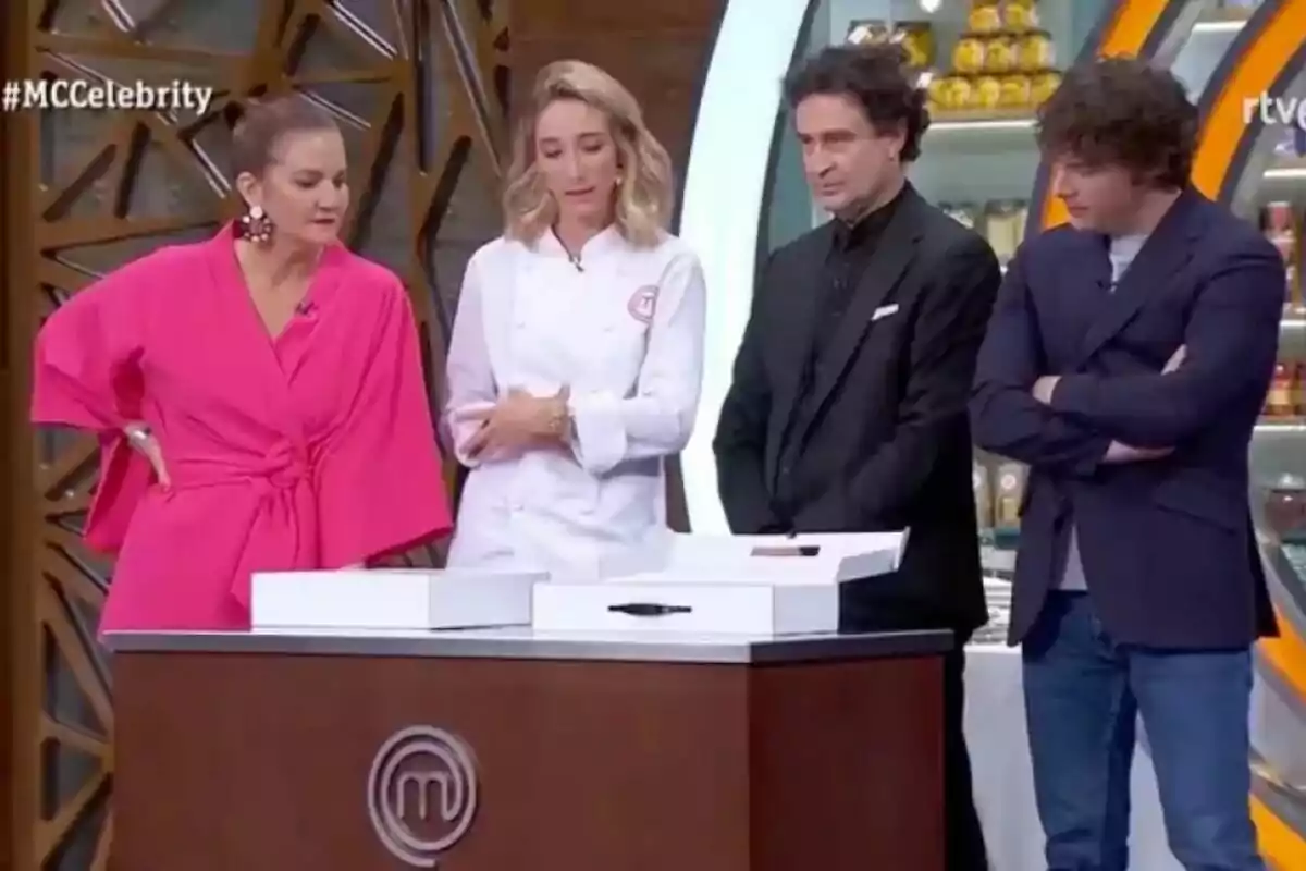 Un grupo de personas formado por Amelicious, Samantha Vallejo-Nágera, Pepe Rodríguez y Jordi Cruz está de pie alrededor de una mesa en un set de televisión, observando atentamente algo frente a ellos en MasterChef. Un grupo de personas formado por Amelicious, Samantha Vallejo-Nágera, Pepe Rodríguez y Jordi Cruz está de pie alrededor de una mesa en un set de televisión, observando atentamente algo frente a ellos en MasterChef.