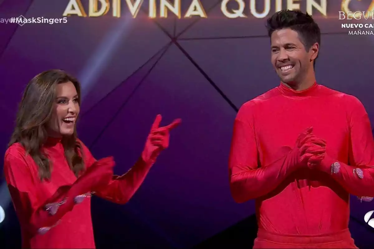 Ana Boyer y Fernando Verdasco vestidas con trajes rojos sonríen en un escenario de Mask Singer con el texto 