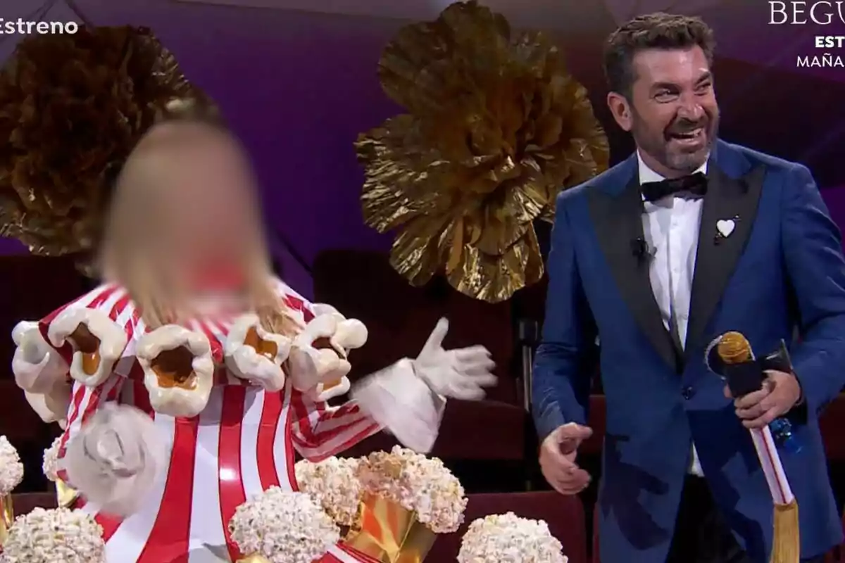 Ana Obregón disfrazada de palomitas de maíz junto a Arturo Valls con esmoquin azul en un escenario decorado con flores doradas en Mask Singer.