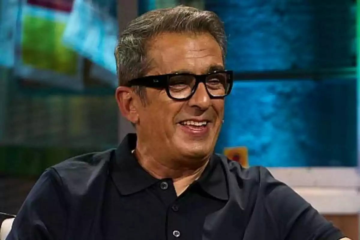 Andreu Buenafuente con gafas y camisa oscura sonríe mientras está sentado en un entorno iluminado en La Revuelta.