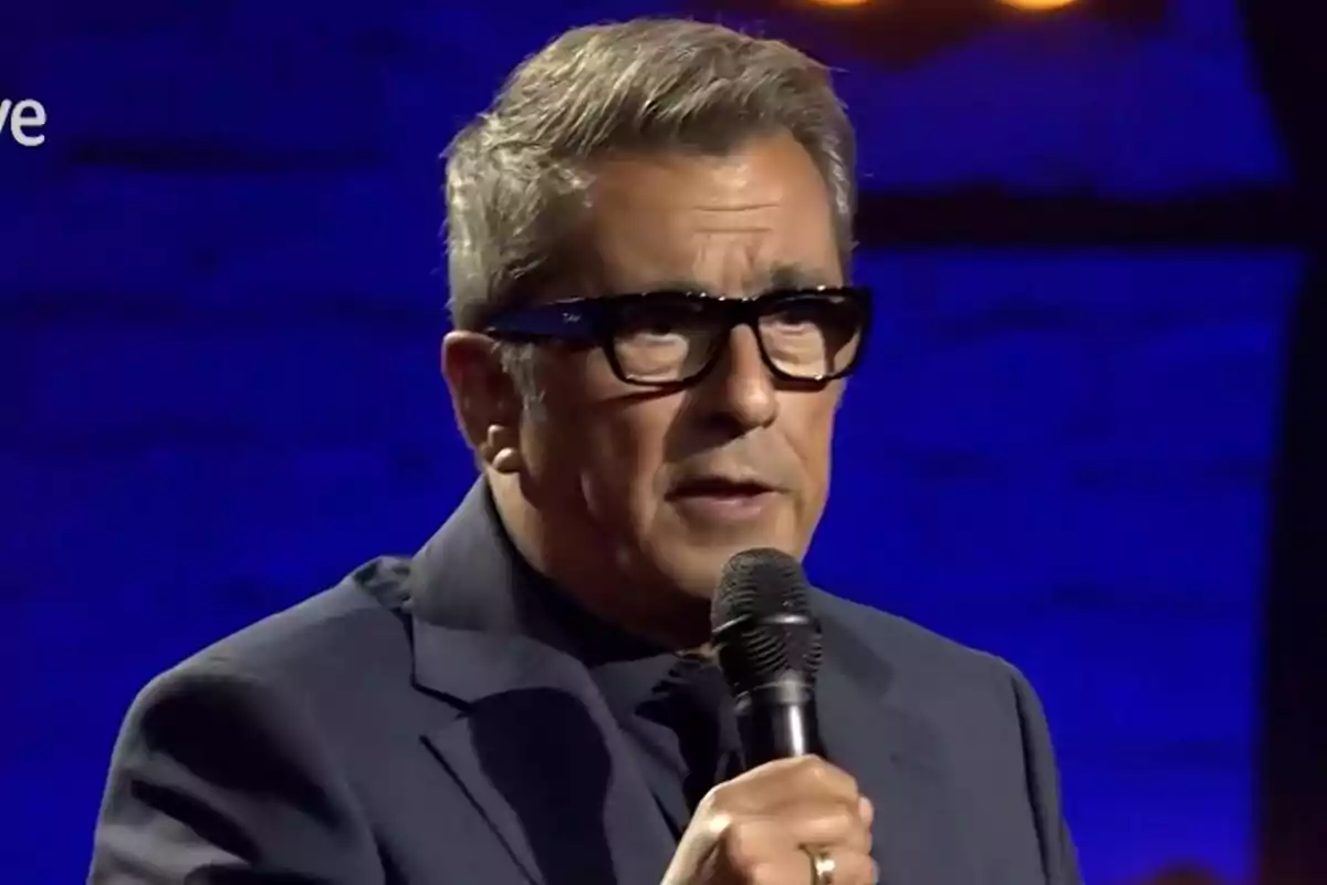 Andreu Buenafuente con gafas y cabello canoso hablando al micrófono en un escenario con fondo azul en Futuro Imperfecto.