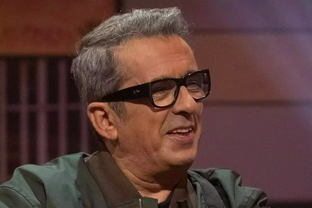 Andreu Buenafuente con gafas negras y cabello canoso sonríe mientras está sentado en un ambiente interior en Al cielo con ella.