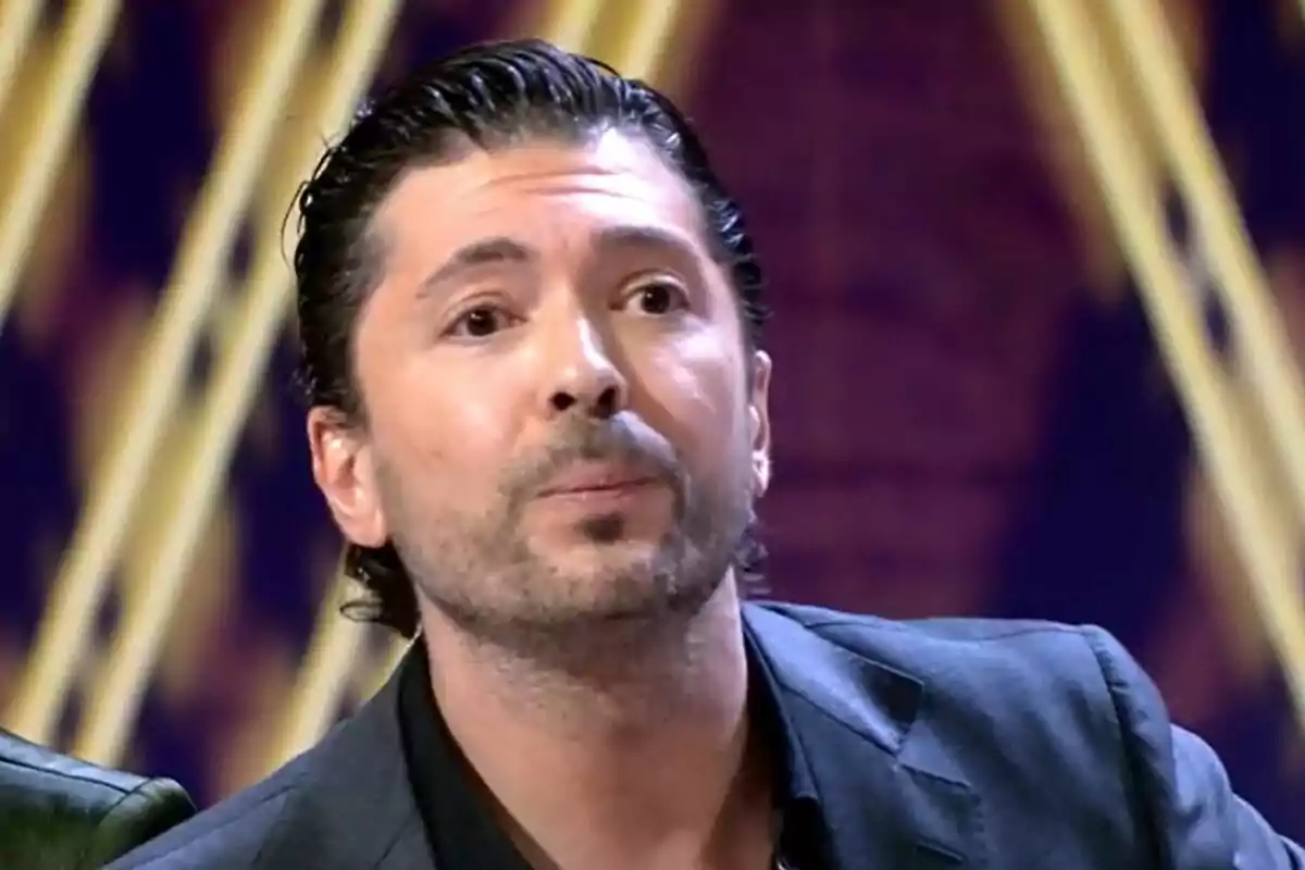 Primer plano de Ángel Cristo JR con actitud enfadada en el plató de De Viernes con fondo morado.
