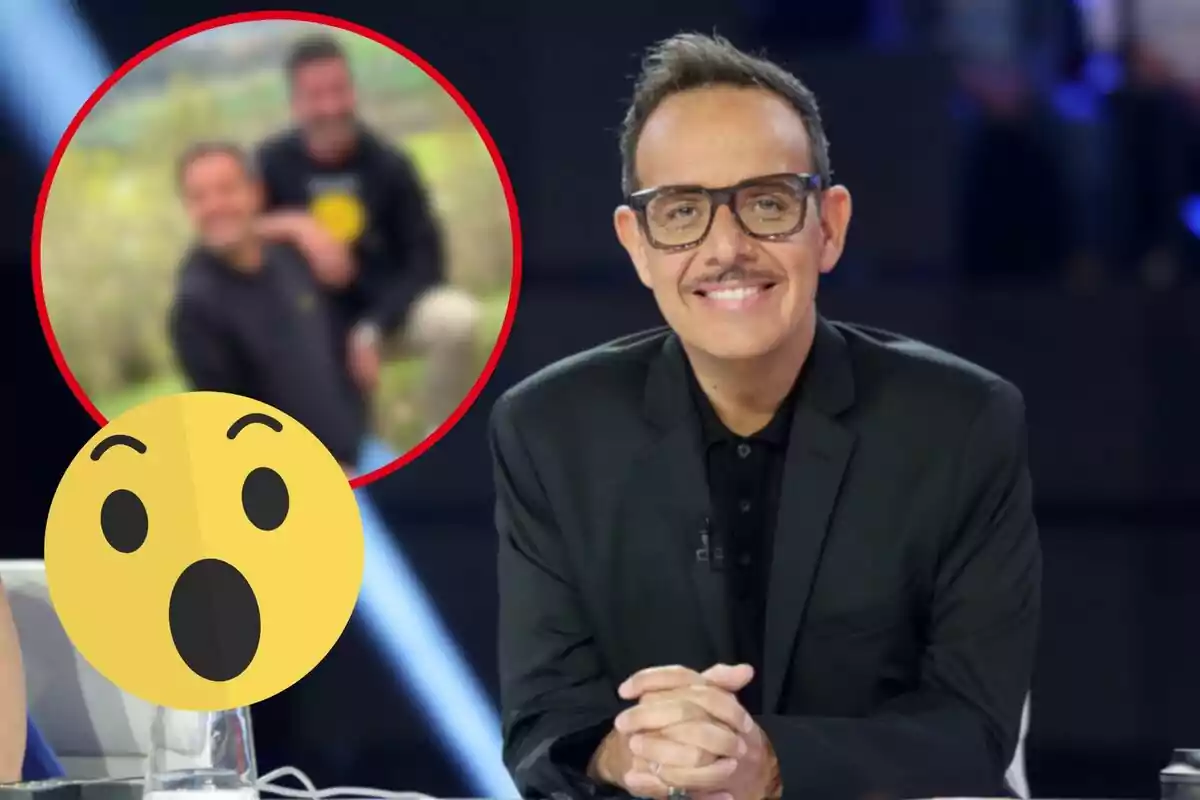 Un hombre con gafas y bigote sonríe mientras está sentado en un estudio de televisión, con una imagen borrosa de dos personas en un círculo rojo y un emoji de sorpresa en la esquina inferior izquierda.