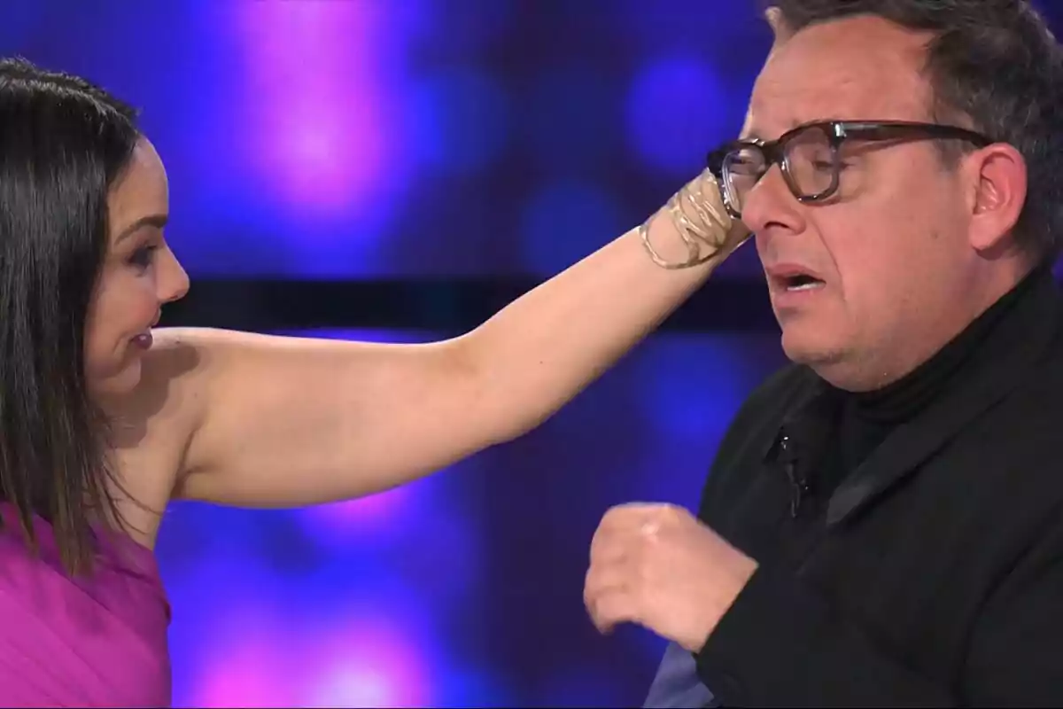 Chenoa toca la cara de Àngel Llàcer con expresión de sorpresa en un fondo de luces azules en Tu Cara Me Suena. Chenoa toca la cara de Àngel Llàcer con expresión de sorpresa en un fondo de luces azules en Tu Cara Me Suena.