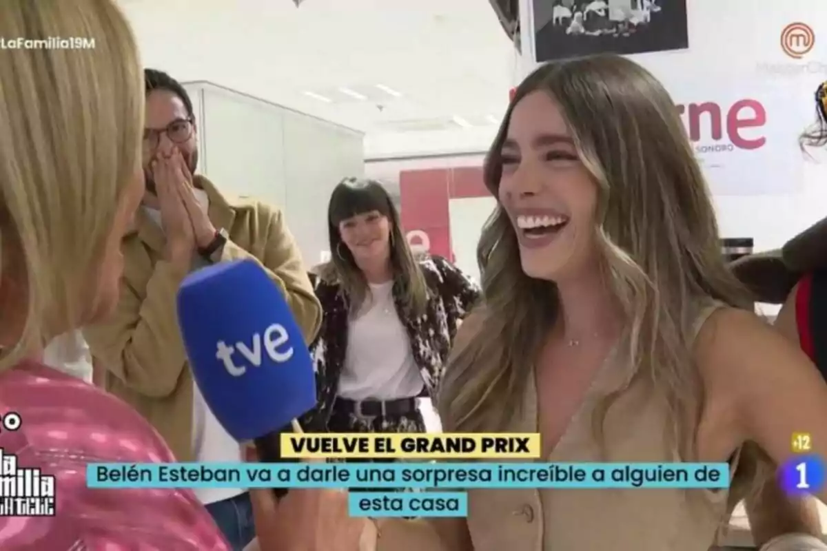 Ángela Fernández sonriente sostiene un micrófono de TVE mientras conversa con otras personas que parecen sorprendidas y felices en un entorno interior. Ángela Fernández sonriente sostiene un micrófono de TVE mientras conversa con otras personas que parecen sorprendidas y felices en un entorno interior.