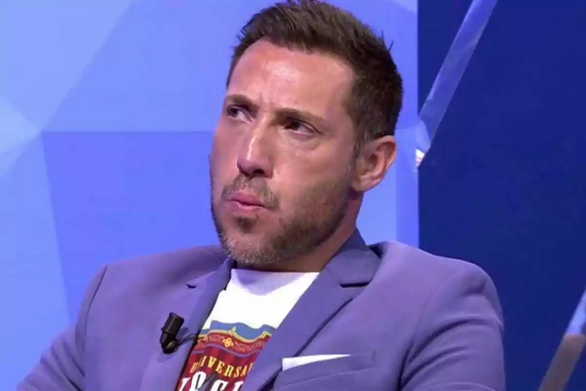 Antonio David Flores con barba y cabello corto lleva una chaqueta azul y una camiseta blanca mientras está sentado en un estudio de televisión en Sálvame. Antonio David Flores con barba y cabello corto lleva una chaqueta azul y una camiseta blanca mientras está sentado en un estudio de televisión en Sálvame.