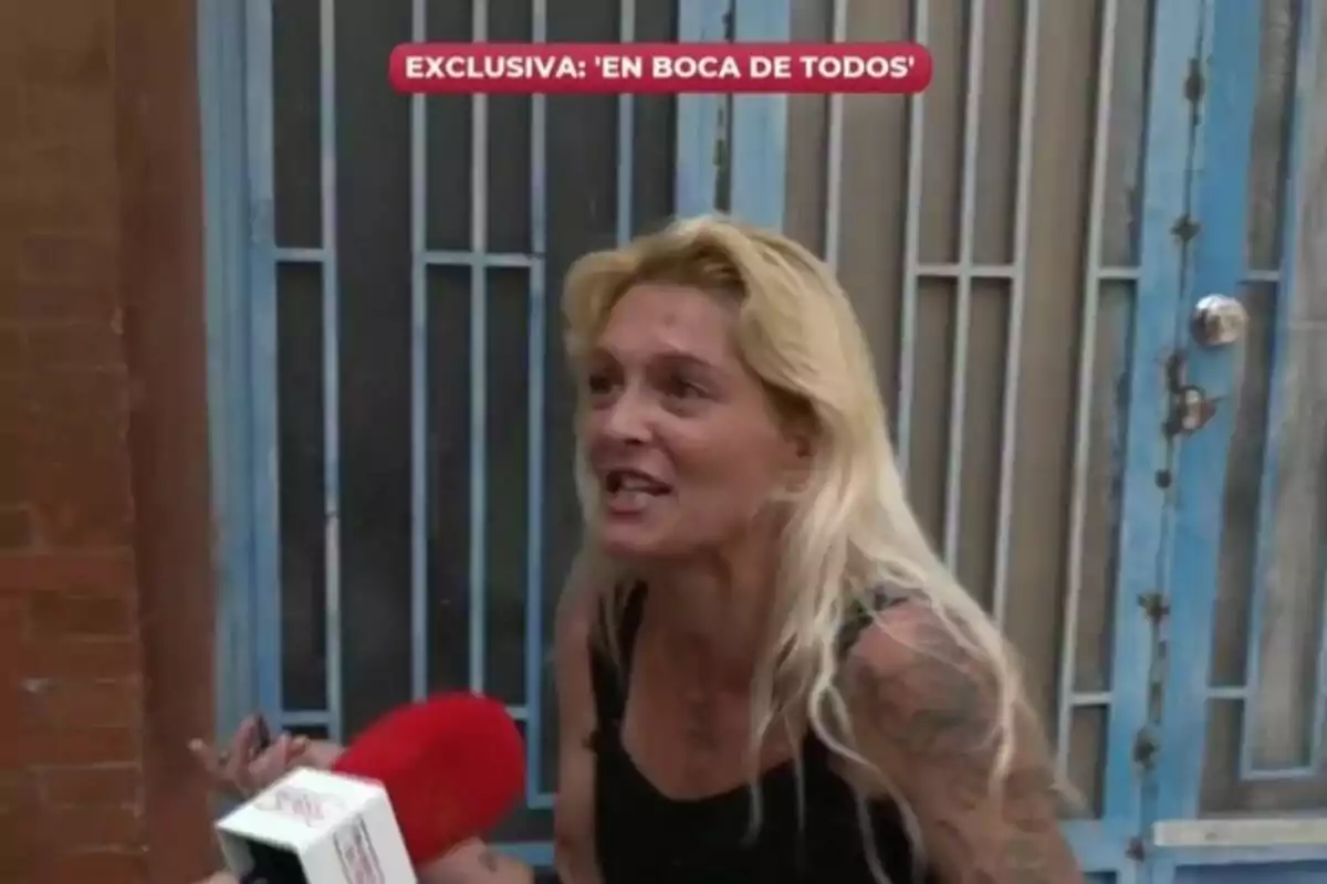 Captura de una mujer rubia con tatuajes siendo entrevistada por En boca de todos frente a una puerta azul.