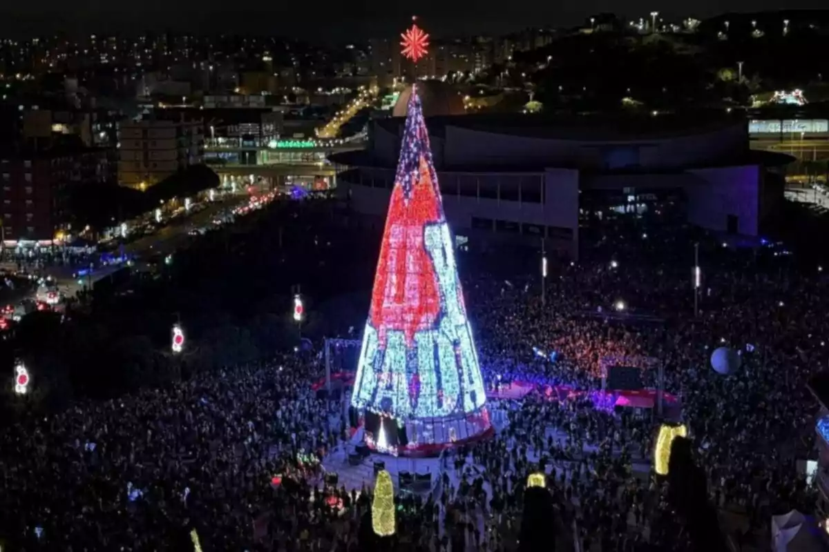 Una multitud se reúne alrededor de un gran árbol de Navidad iluminado en una ciudad durante la noche.