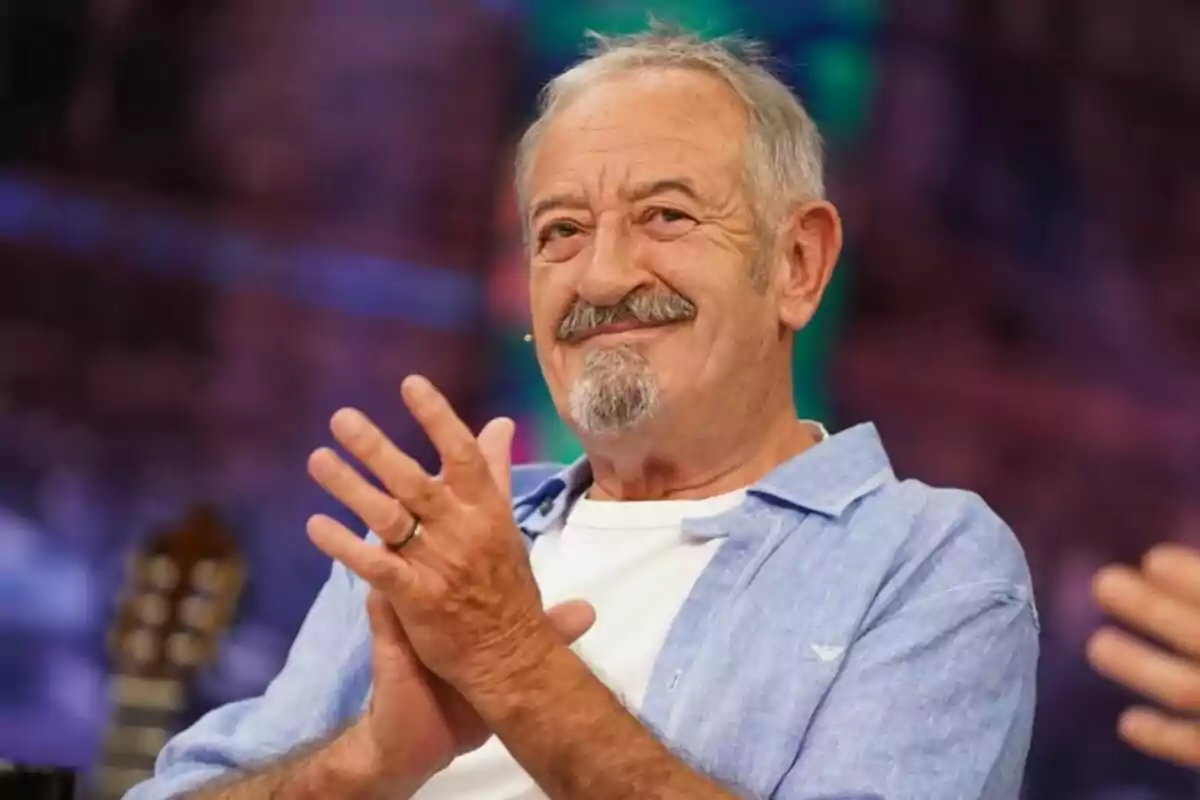 Karlos Arguiñano con barba y bigote sonríe y aplaude mientras está sentado en un ambiente colorido en 'El Hormiguero'.