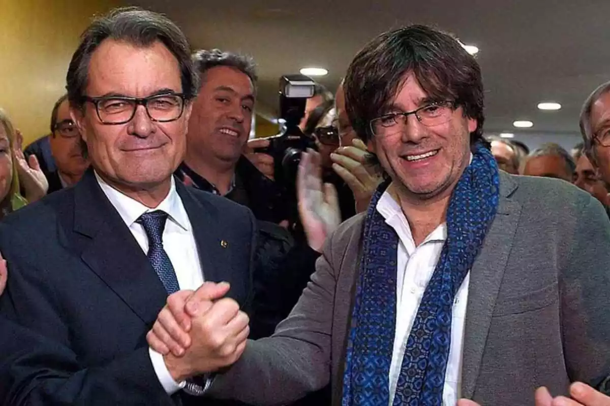 Artur Mas con Carles Puigdemont dándose la mano con fotógrafos a su alrededor