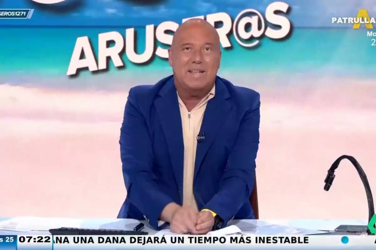 Alfonso Arús con chaqueta azul y camisa beige está sentado detrás de un escritorio, con un micrófono a su derecha y un fondo que dice "ARUSER@S". Captura de 'Aruser@s' el 25 de junio de 2024