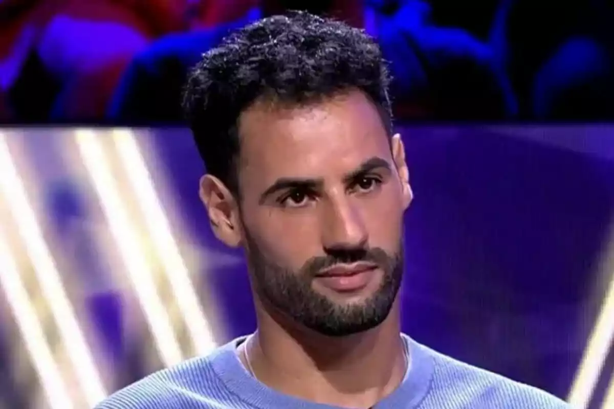 Asraf Beno con barba y cabello oscuro en un el plató de De Viernes con luces de colores.