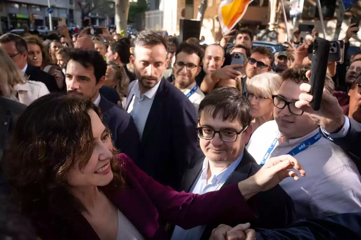 Plano general con Isabel Díaz Ayuso en primer plano sonriendo rodeada de decenas de personas