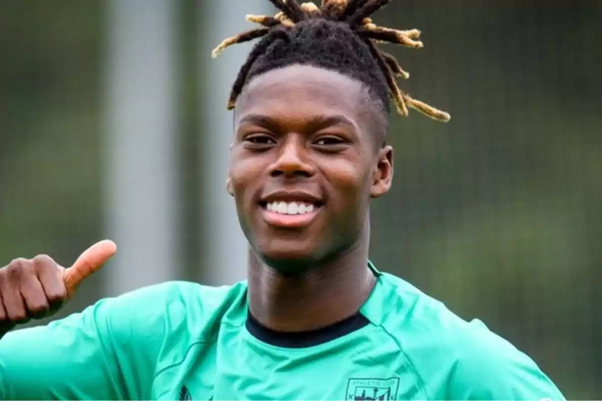 Un joven futbolista sonriente con una camiseta verde y el pulgar levantado.