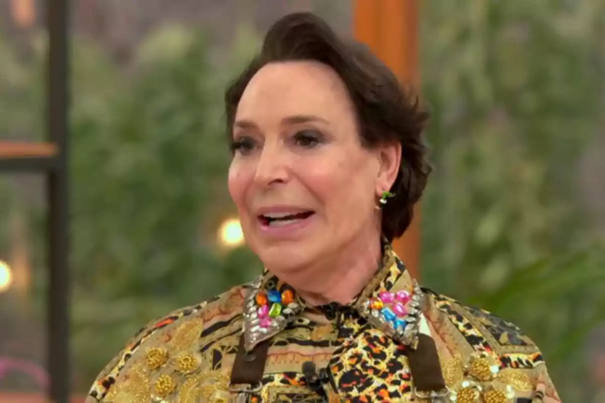 Benita lleva una camisa con un diseño colorido y adornos brillantes, en un entorno interior con fondo desenfocado. Captura de 'Bake Off' Benita lleva una camisa con un diseño colorido y adornos brillantes, en un entorno interior con fondo desenfocado. Captura de 'Bake Off'