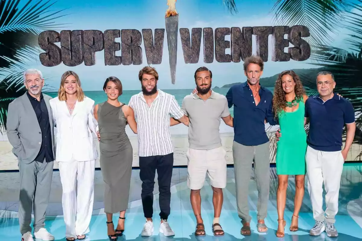 Carlos Sobera, Sandra Barneda, Anita Williams, Montoya, Borja González, Álvaro Muñoz Escassi, Laura Madrueño y Jorge Javier Vázquez personas posan sonrientes frente a un cartel de Supervivientes con fondo de playa y palmeras