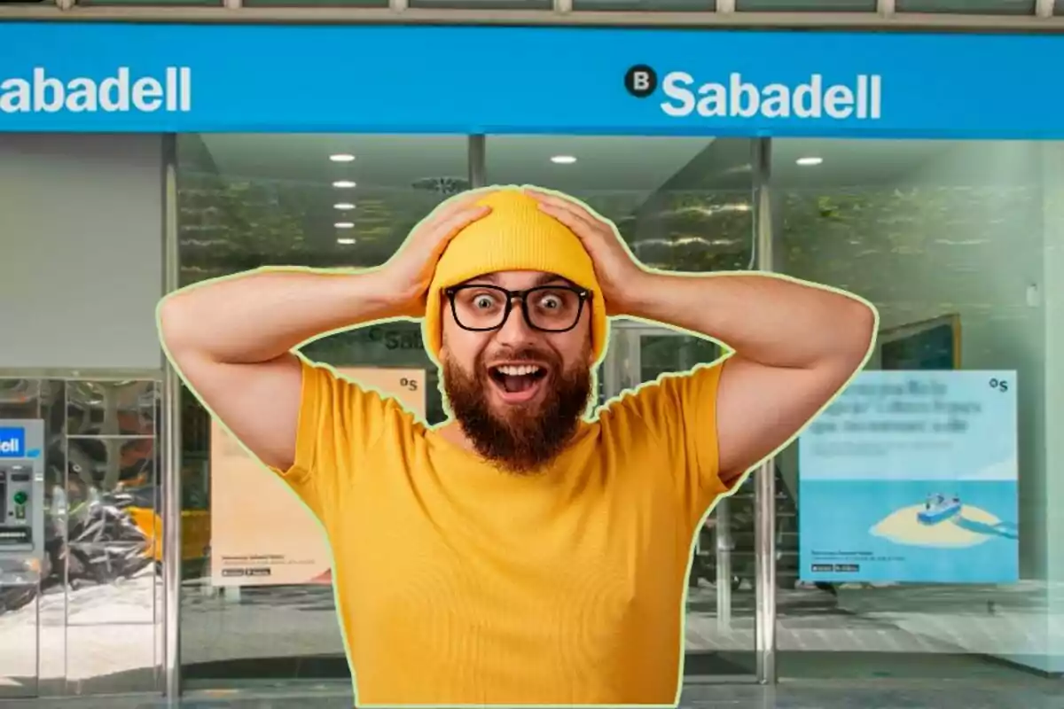 Un hombre con gorro y camiseta amarillos, con expresión de sorpresa, frente a una sucursal del banco Sabadell.