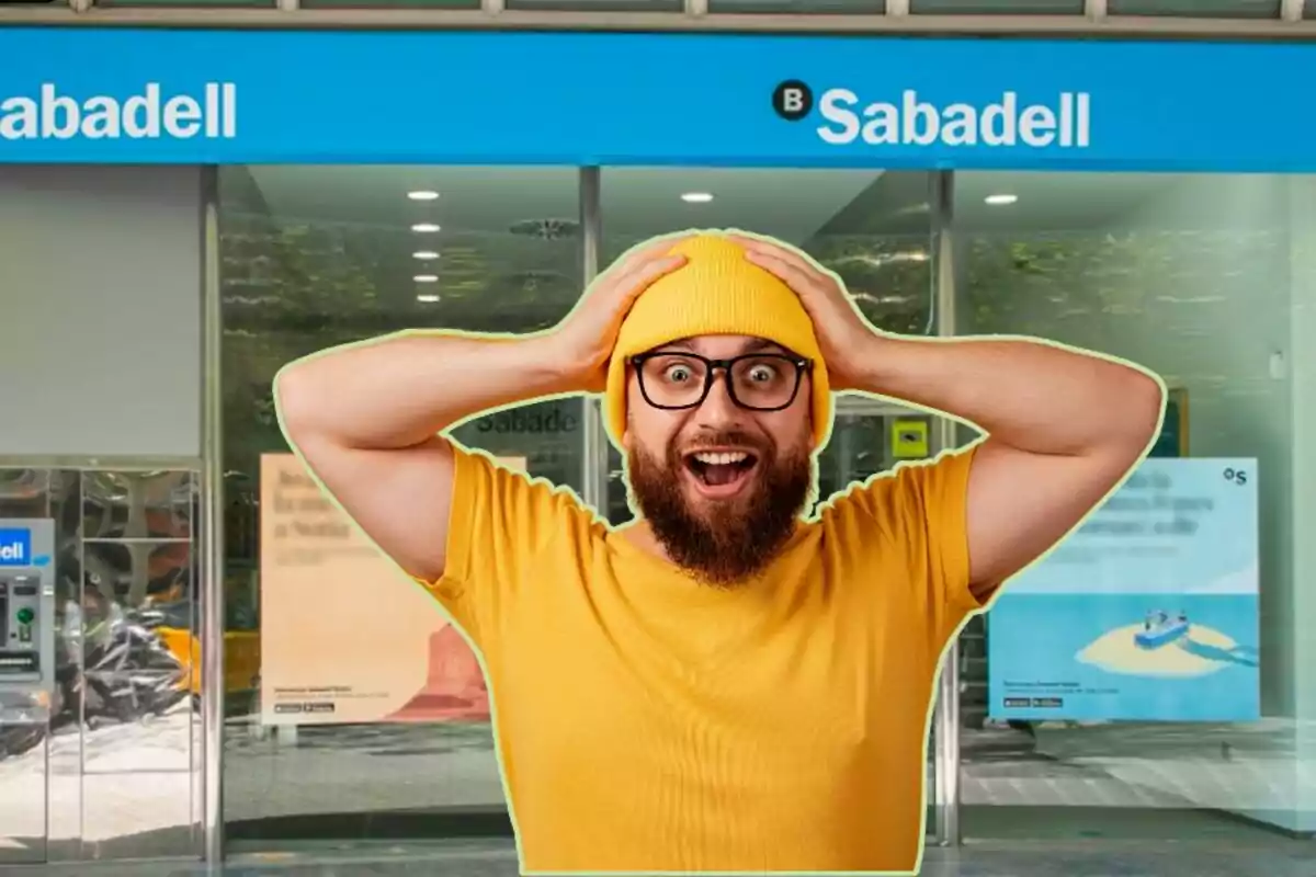 Un hombre con gorro y camiseta amarillos, con expresión de sorpresa, frente a una sucursal del banco Sabadell.