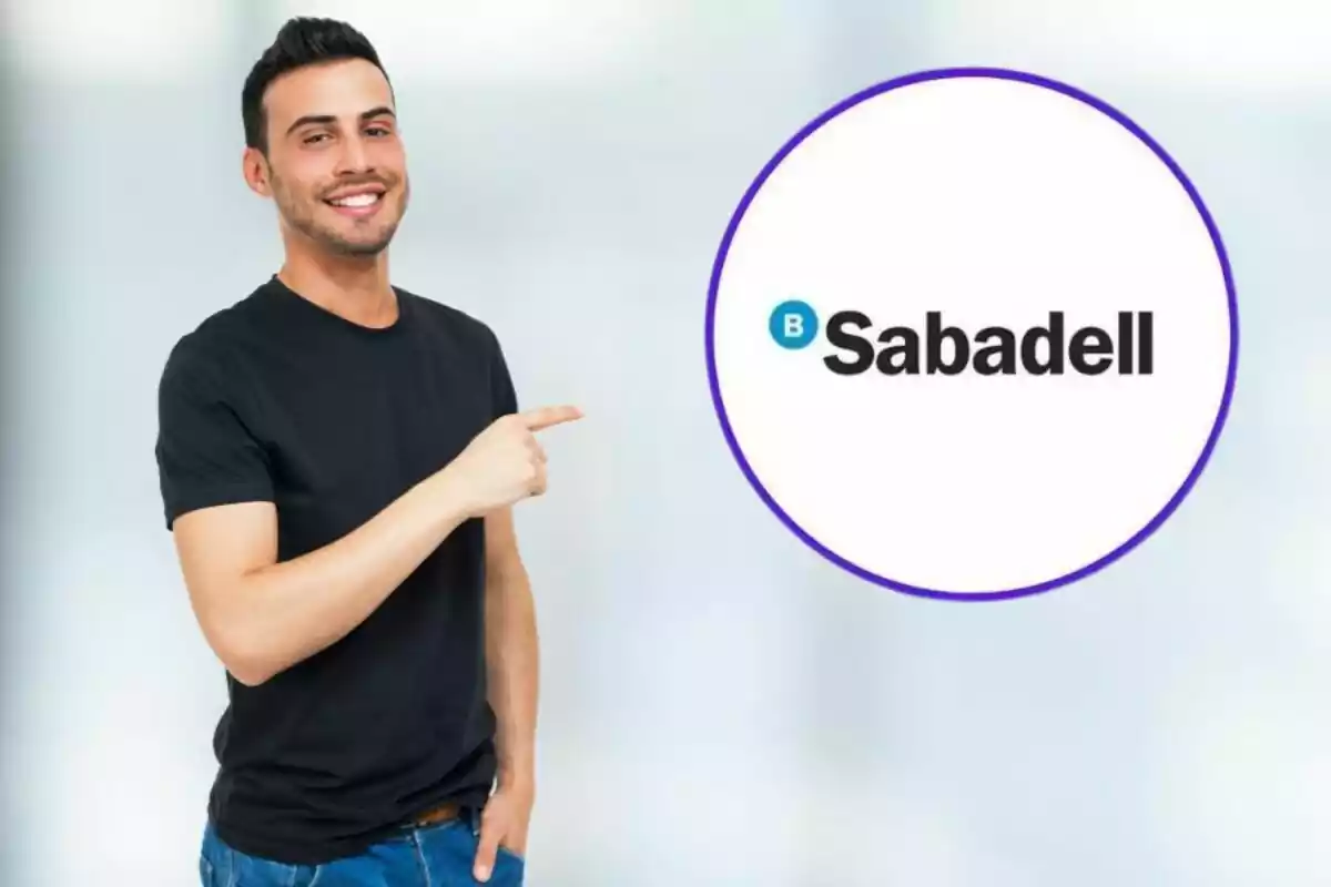 Un hombre sonriente con camiseta negra y jeans señala con su dedo índice derecho hacia el logotipo de Sabadell dentro de un círculo púrpura.