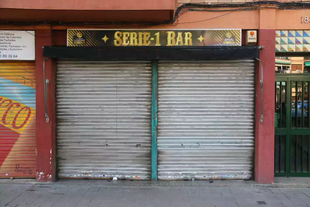 Imagen frontal del bar Serie-1 Dominicano de Badalona con las persianas bajadas