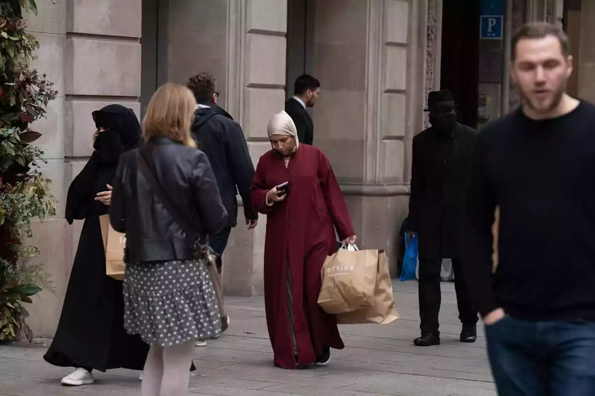 Varias personas andando por la calle de Barcelona, dos de ellas son mujeres con velo y bruka