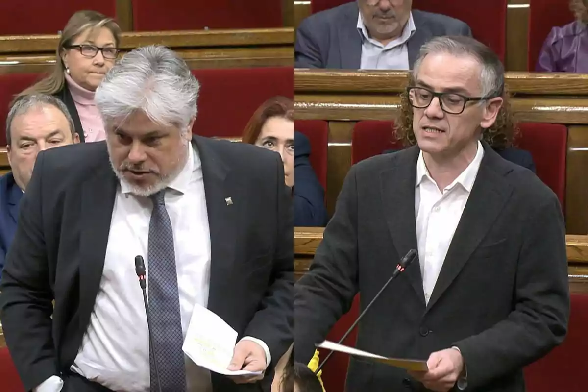 Dos hombres de pie en un parlamento, uno con cabello canoso y barba, el otro con gafas y cabello corto, ambos sosteniendo papeles mientras hablan.