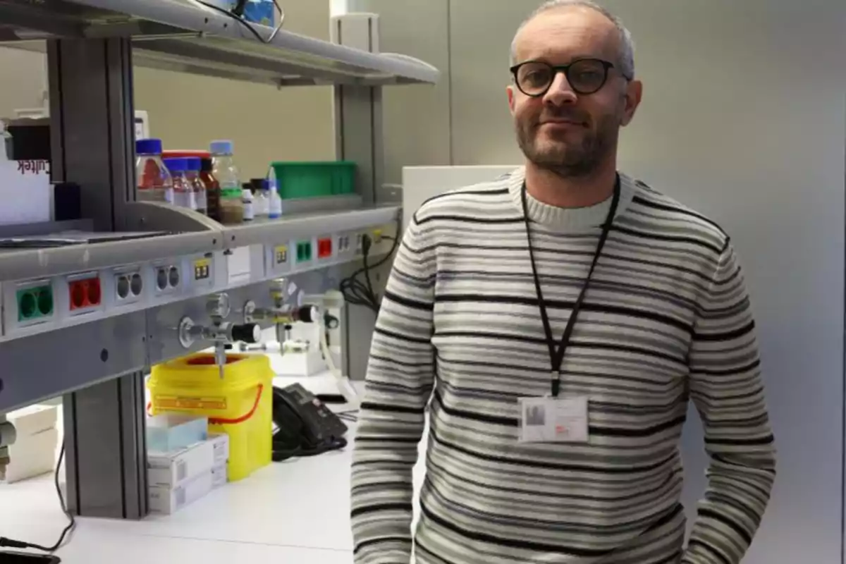 Hombre con gafas y suéter de rayas en un laboratorio con equipo y suministros científicos.