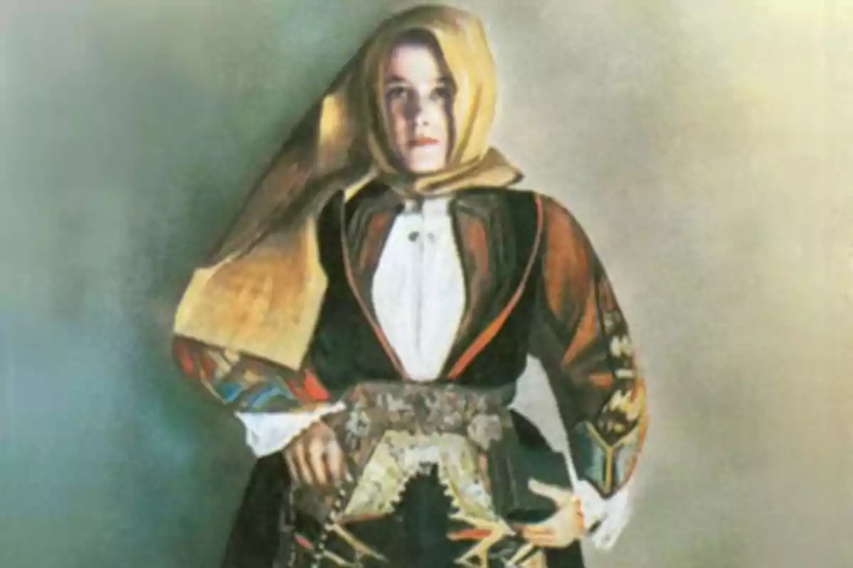 Una persona vestida con un traje tradicional que incluye un pañuelo en la cabeza y una chaqueta decorada, posando con las manos en la cintura. Una persona vestida con un traje tradicional que incluye un pañuelo en la cabeza y una chaqueta decorada, posando con las manos en la cintura.
