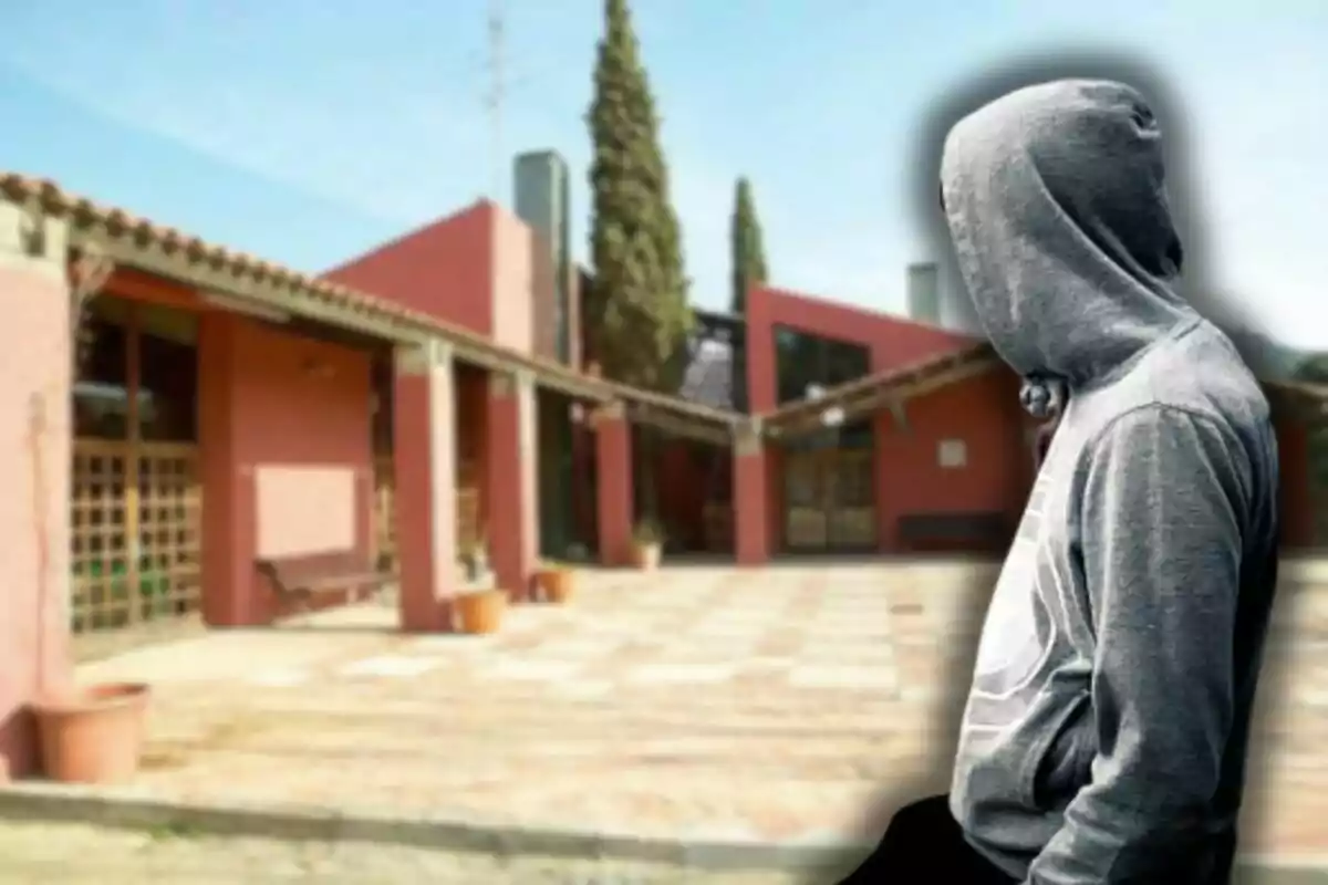 Un edificio de ladrillo rojo con un patio al frente y una persona con sudadera gris con capucha de perfil.