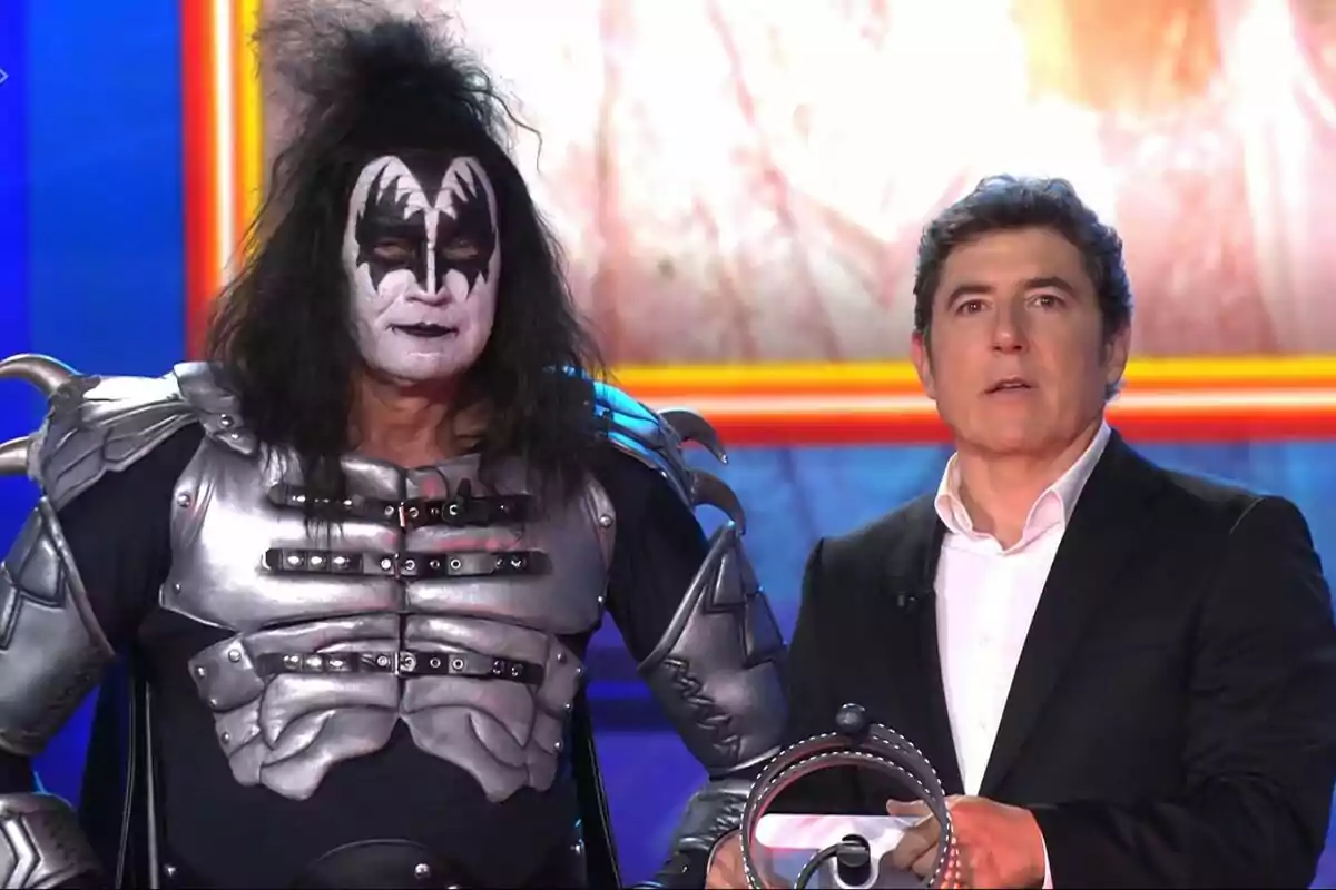 Bertín Osborne y Manel Fuentes en un escenario, una vestida con un traje metálico y maquillaje llamativo, y la otra con traje formal en Tu Cara Me Suena.