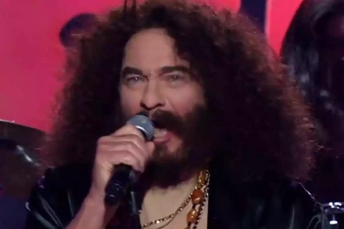 Bertín Osborne con cabello rizado y barba cantando en un escenario de Tu Cara Me Suena mientras sostiene un micrófono