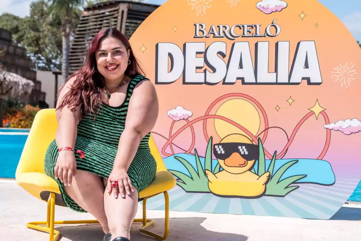Blanca Martínez sentada en una silla amarilla frente a un cartel colorido de Barceló Desalia con un pato animado usando gafas de sol y una piscina al fondo