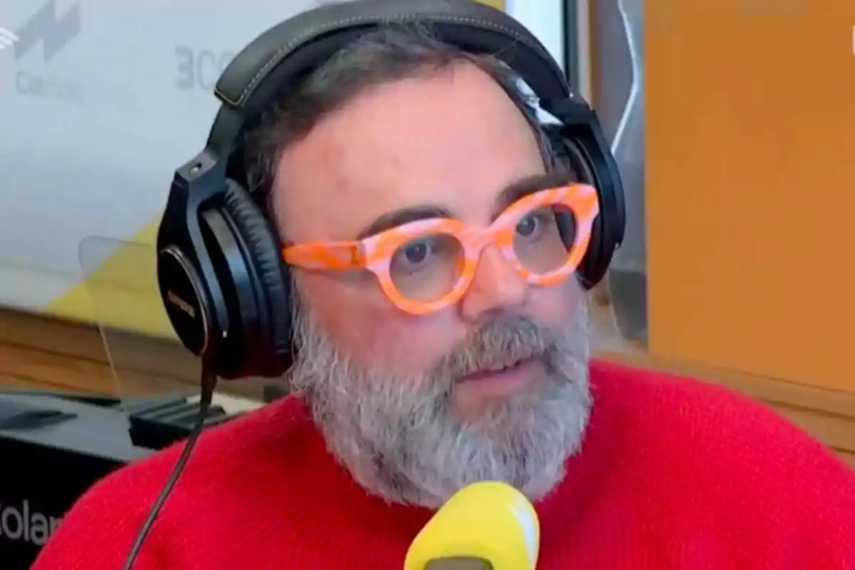 Bob Pop con barba y gafas naranjas usando auriculares grandes y un suéter rojo, hablando frente a un micrófono amarillo en un estudio de Catalunya Ràdio.