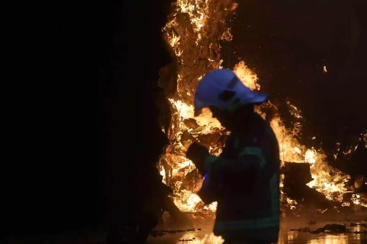 Un bombero, de perfil, con un incendio de fondo