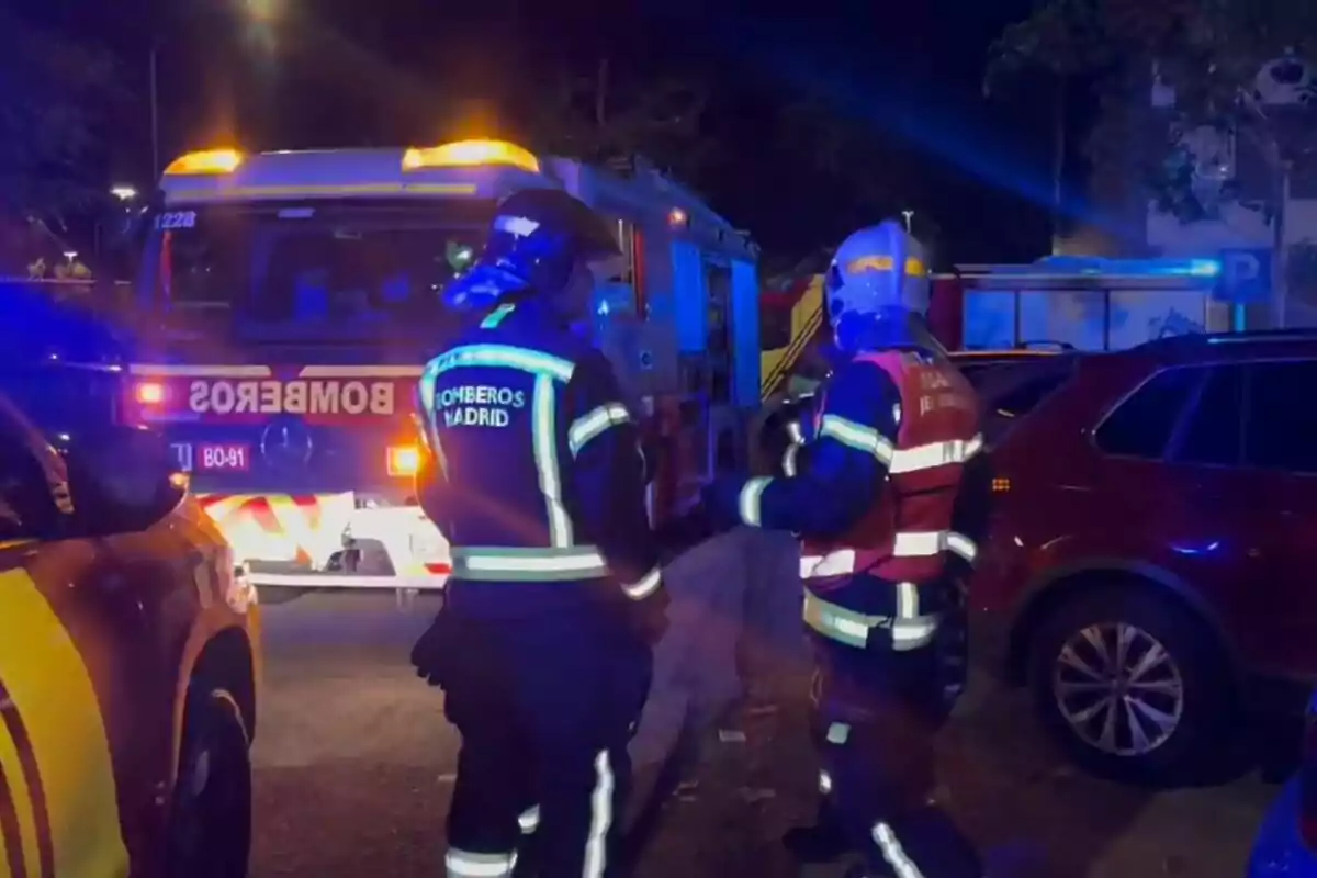 Bomberos de Madrid trabajando de noche junto a un camión de bomberos iluminado.